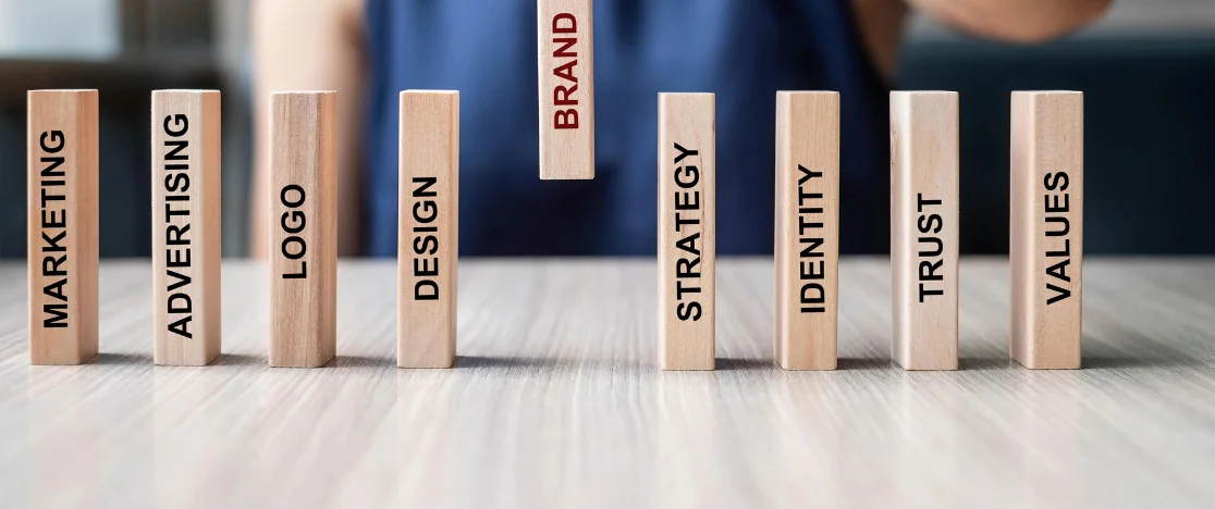 A man focuses on wooden blocks labeled with the brand, marketing, & strategy to increase visibility.