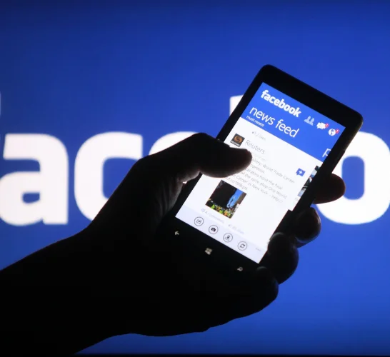 A person with a smartphone in his hand and the Facebook app open displays the news feed on Facebook.