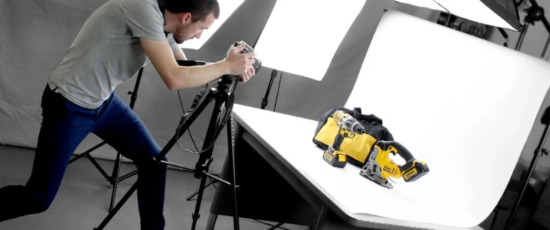 In a brightly lit shooting room, a man is taking product photos of power tools set up on a table.